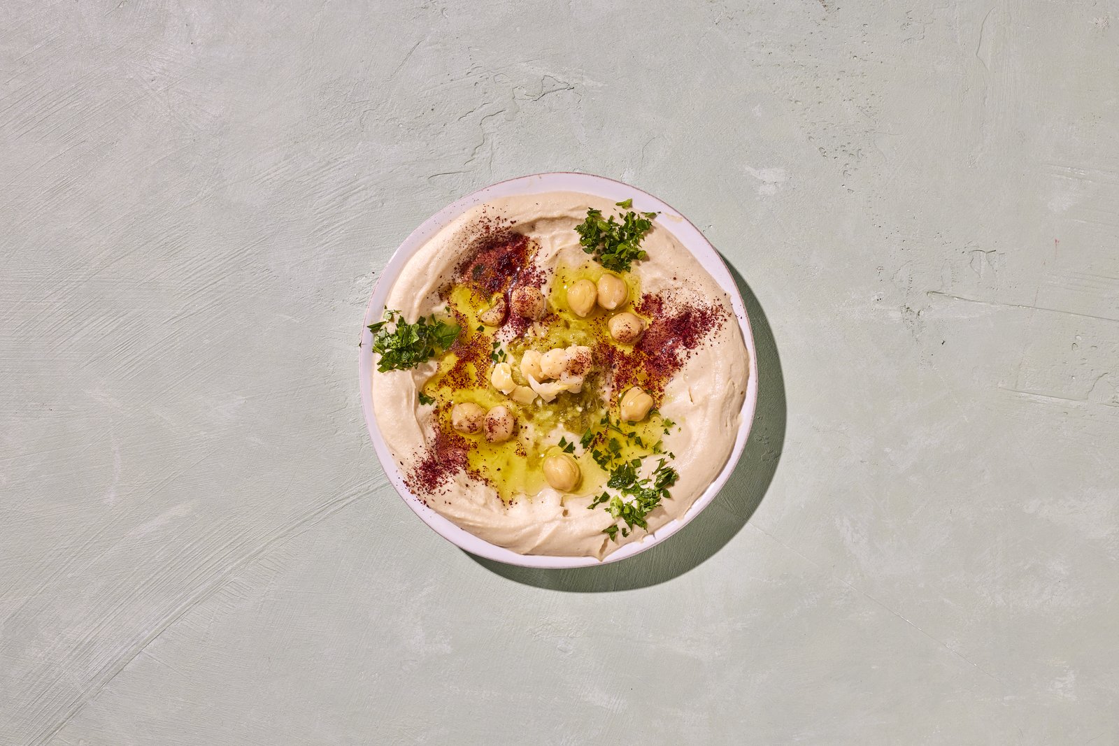 Bowl of creamy hummus topped with chickpeas, olive oil, sumac and parsley
