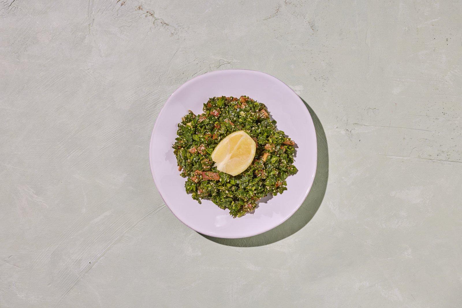 Plate of tabbouleh — finely chopped parsley, tomato and bulgur with a lemon wedge