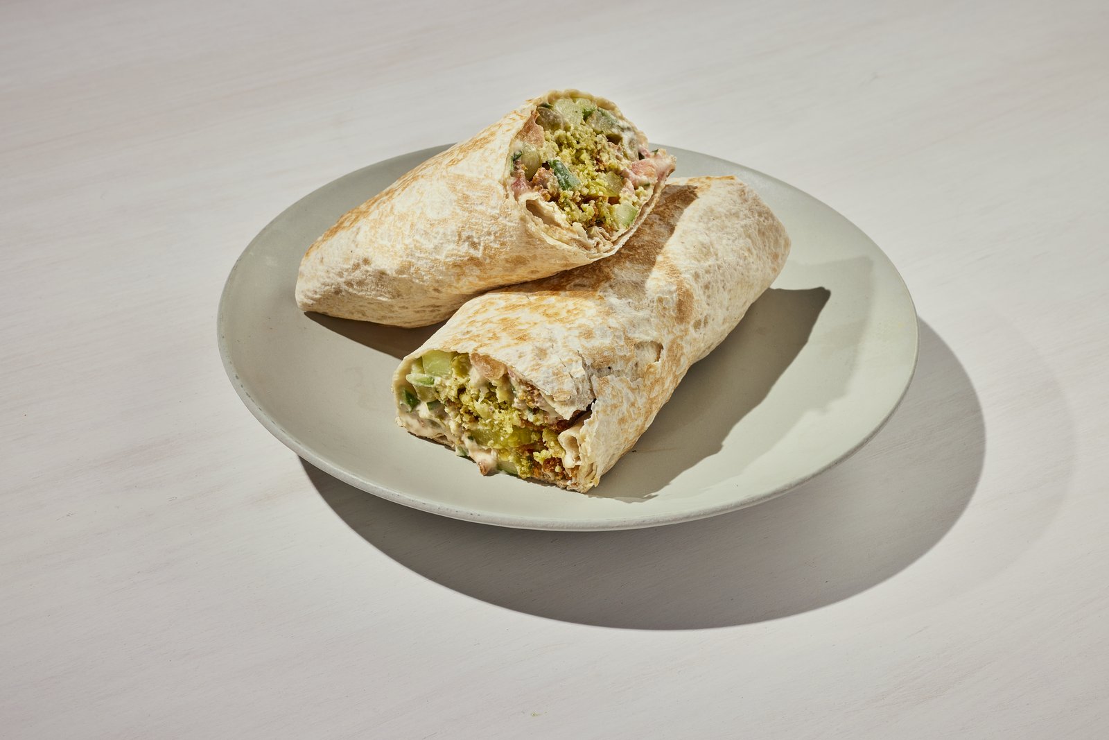 Falafel wrap cut in half showing falafel, cucumber, tomato and tahini