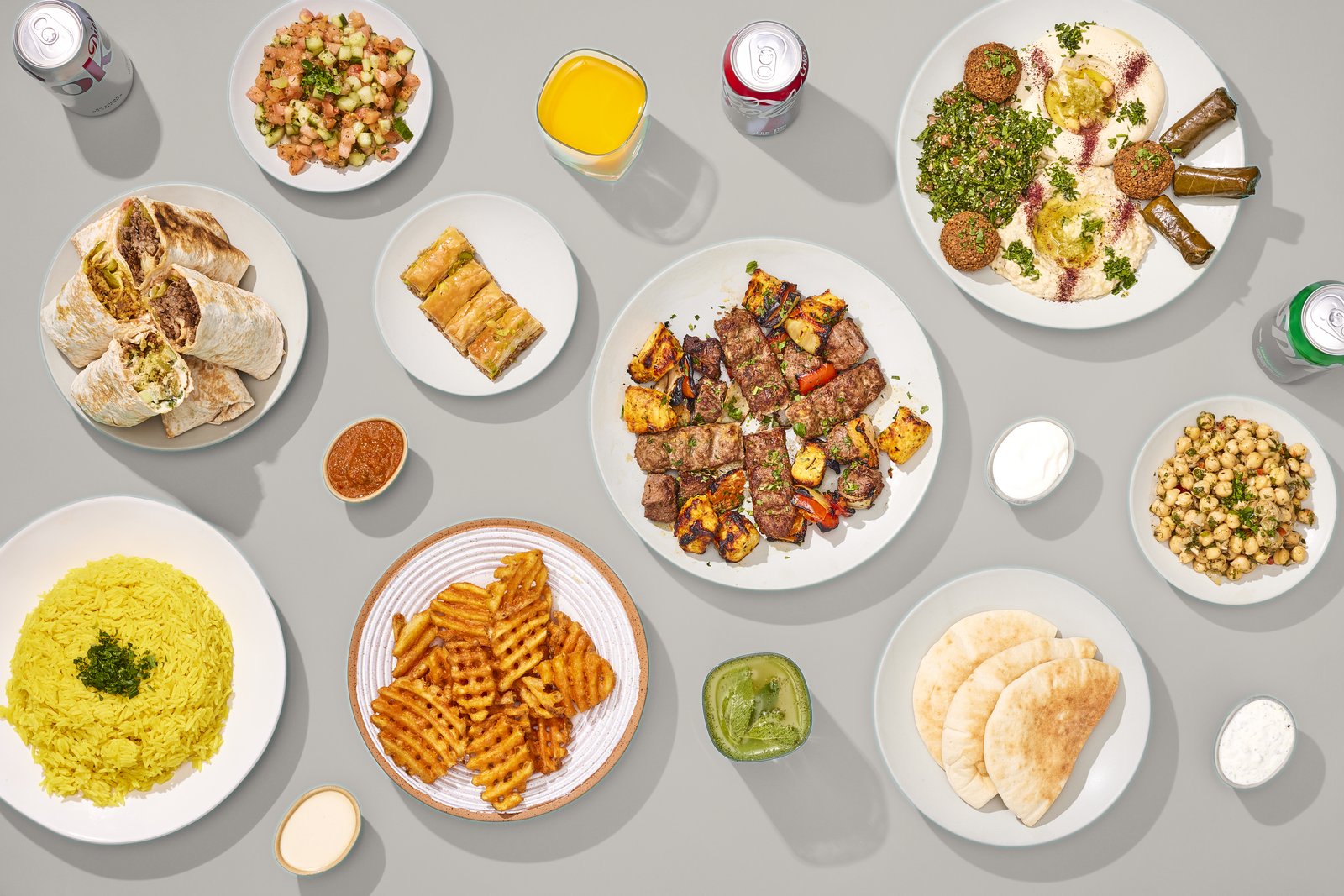A full Sinya spread — kabobs, wraps, hummus, tabbouleh, salads, rice, fries, pita, baklava and drinks