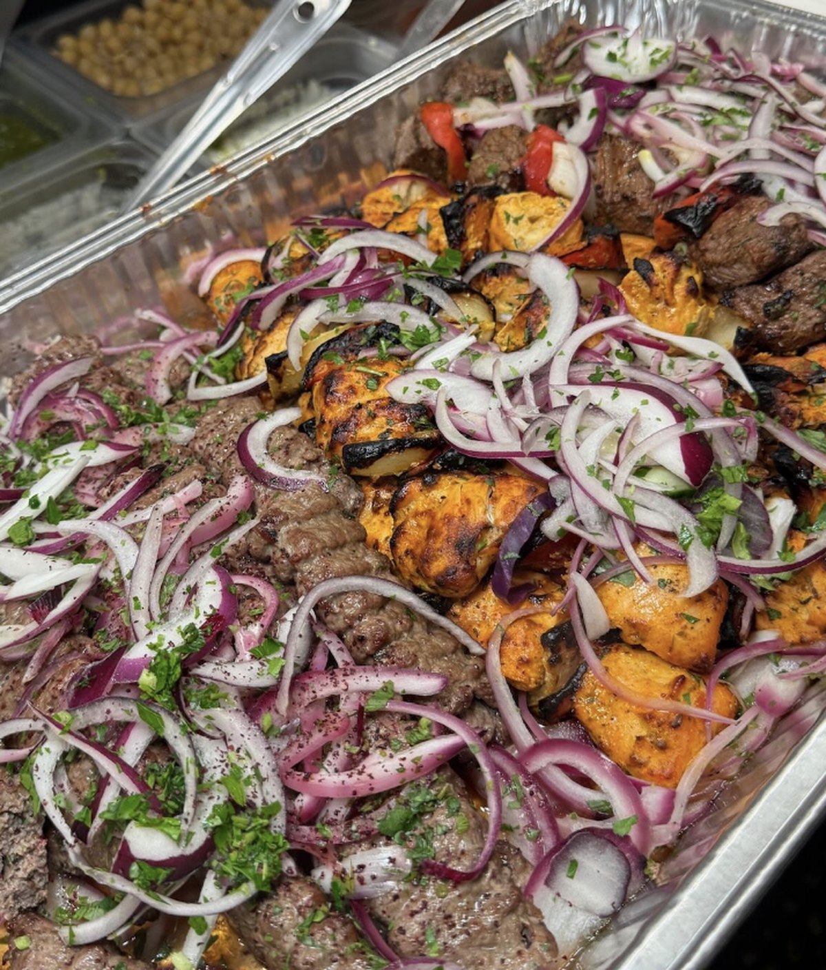 Full catering tray of chicken, beef and kafta kabobs topped with sumac onions and parsley